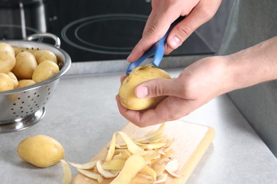 Photo of Man peeling fresh potato at grey countertop in kitchen, closeup