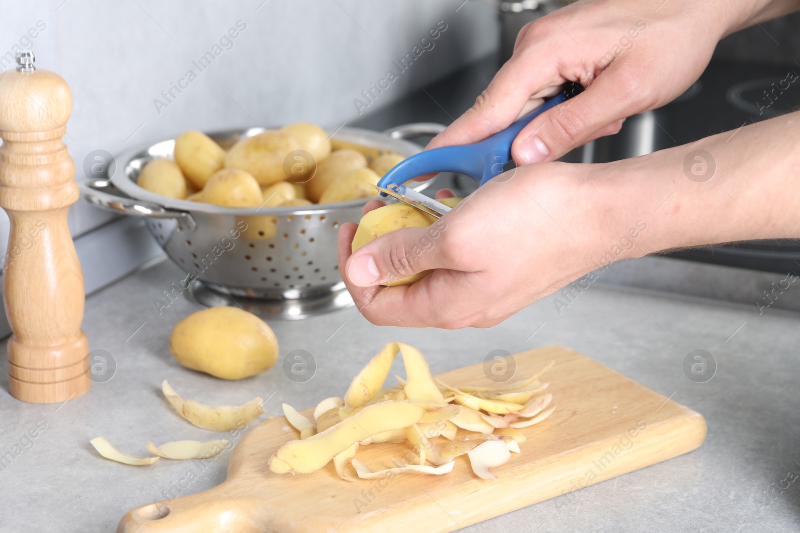 Photo of Man peeling fresh potato at grey countertop in kitchen, closeup