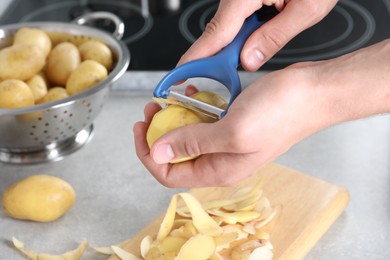 Man peeling fresh potato at grey countertop in kitchen, closeup