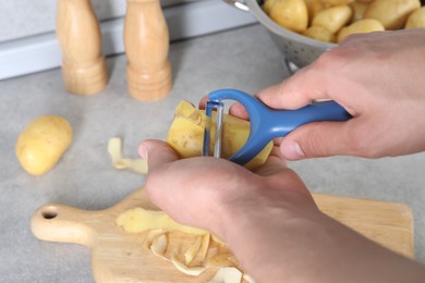 Photo of Man peeling fresh potato at grey countertop in kitchen, closeup