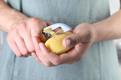 Photo of Man peeling fresh potato with peeler, closeup