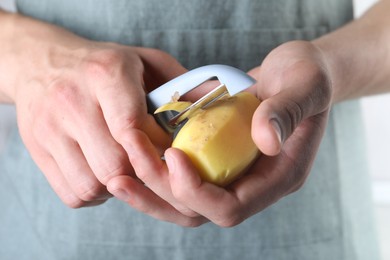 Photo of Man peeling fresh potato with peeler, closeup