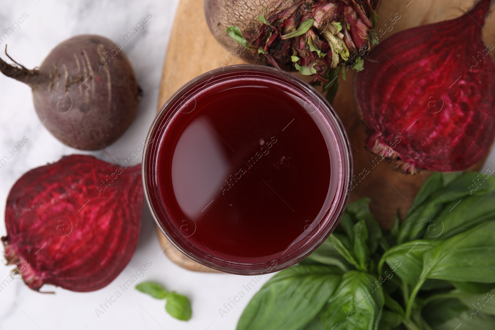 Photo of Fresh beet juice in glass, ripe vegetables and basil on light table, flat lay