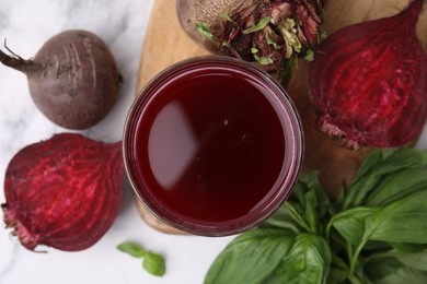 Fresh beet juice in glass, ripe vegetables and basil on light table, flat lay