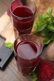 Photo of Fresh beet juice in glasses, ripe vegetables and mint on wooden table, closeup