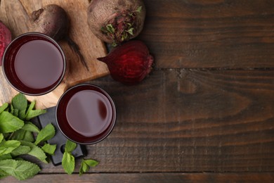 Fresh beet juice in glasses, ripe vegetables and mint on wooden table, flat lay. Space for text