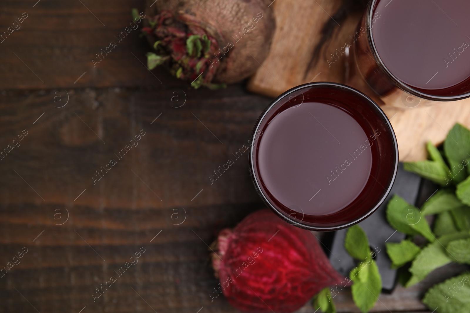 Photo of Fresh beet juice in glasses, ripe vegetables and mint on wooden table, flat lay. Space for text