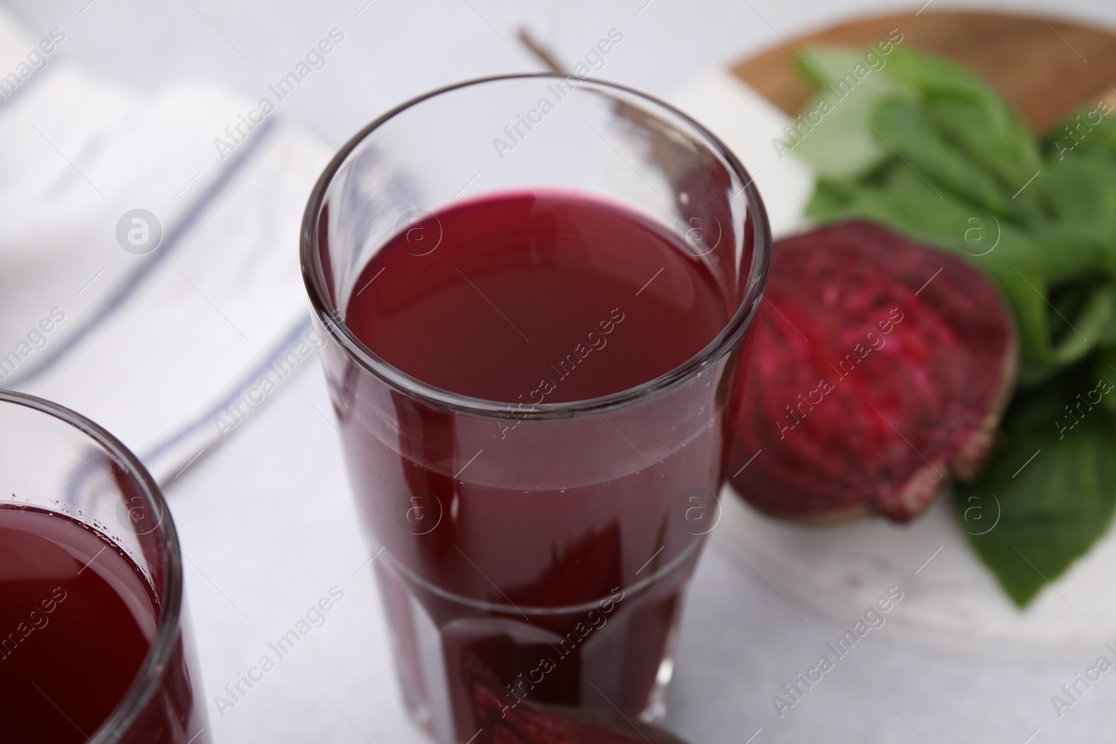 Photo of Fresh beet juice in glasses, ripe vegetable and basil on light table, closeup