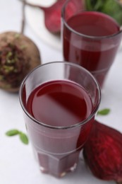 Fresh beet juice in glasses and ripe vegetables on white table, closeup