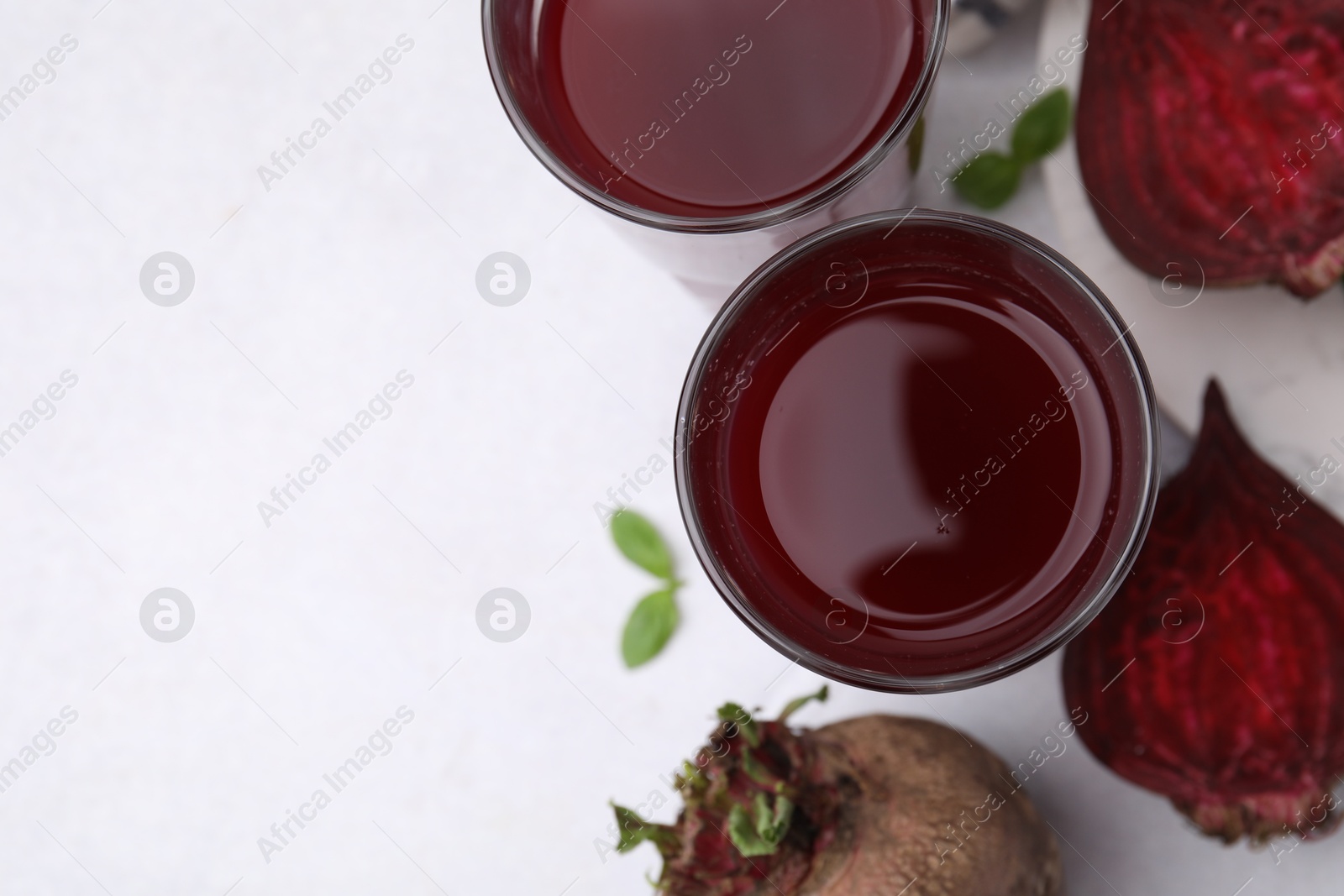 Photo of Fresh beet juice in glass and ripe vegetables on white table, flat lay. Space for text