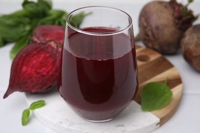 Photo of Fresh beet juice in glass, ripe vegetables and basil on white table, closeup