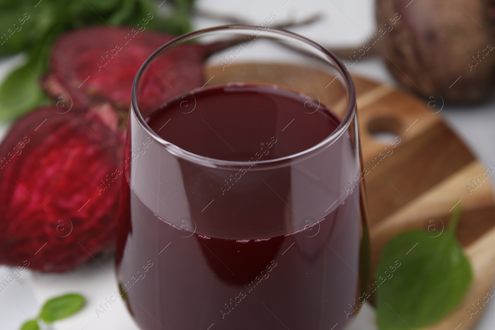 Photo of Fresh beet juice in glass and ripe vegetables on table, closeup