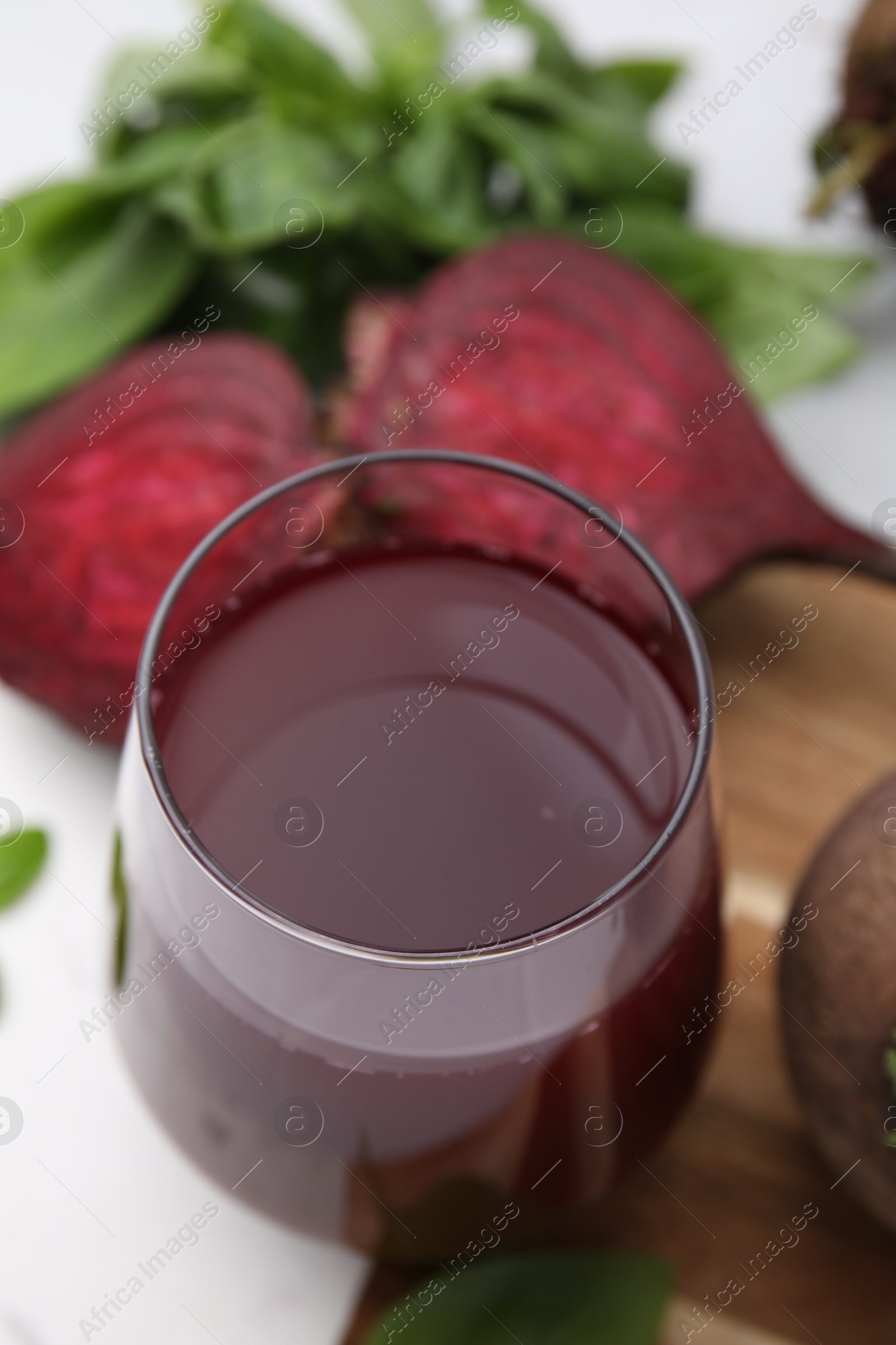 Photo of Fresh beet juice in glass, ripe vegetables and basil on table, closeup