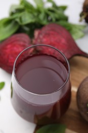 Fresh beet juice in glass, ripe vegetables and basil on table, closeup