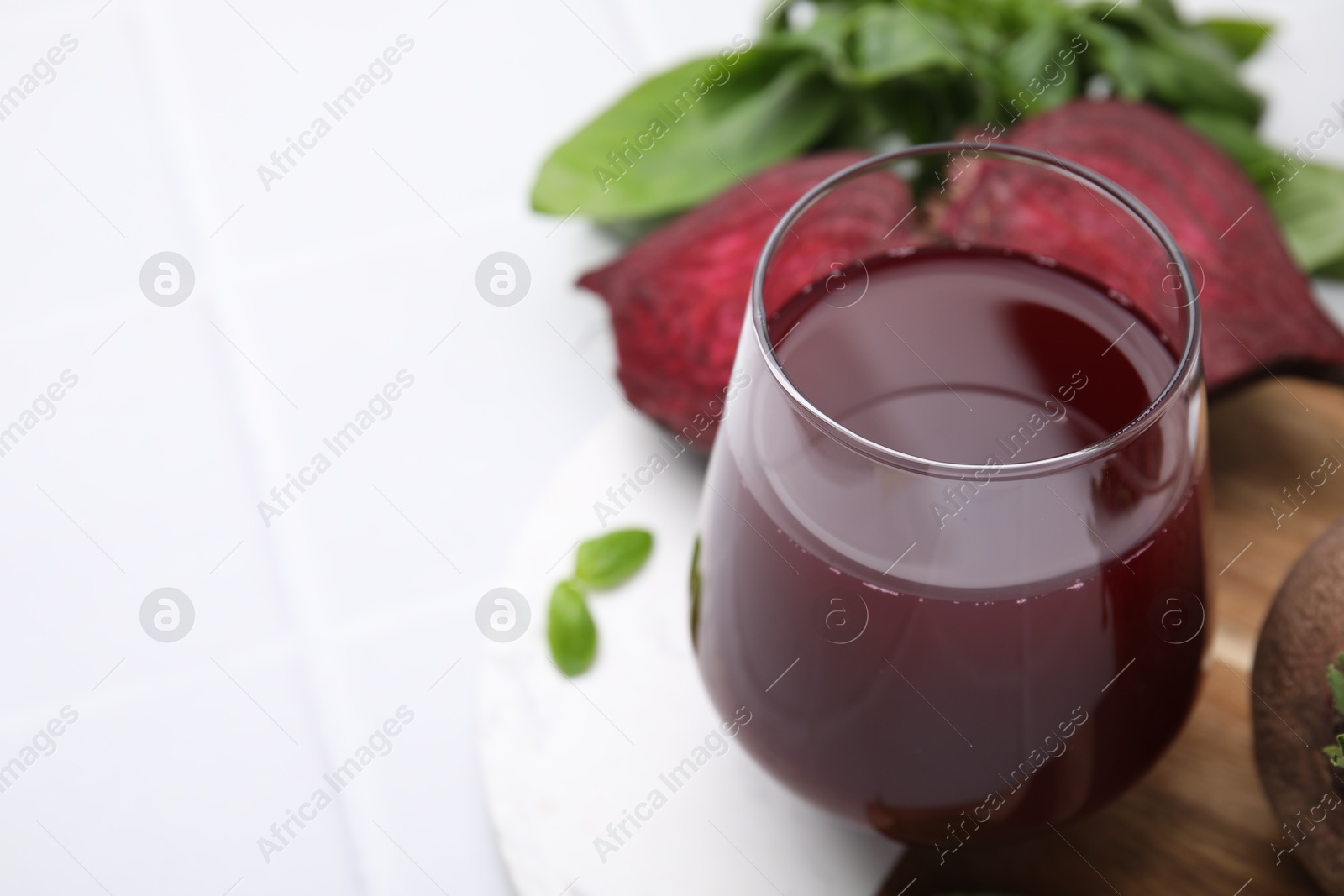 Photo of Fresh beet juice in glass, ripe vegetables and basil on white table, closeup. Space for text