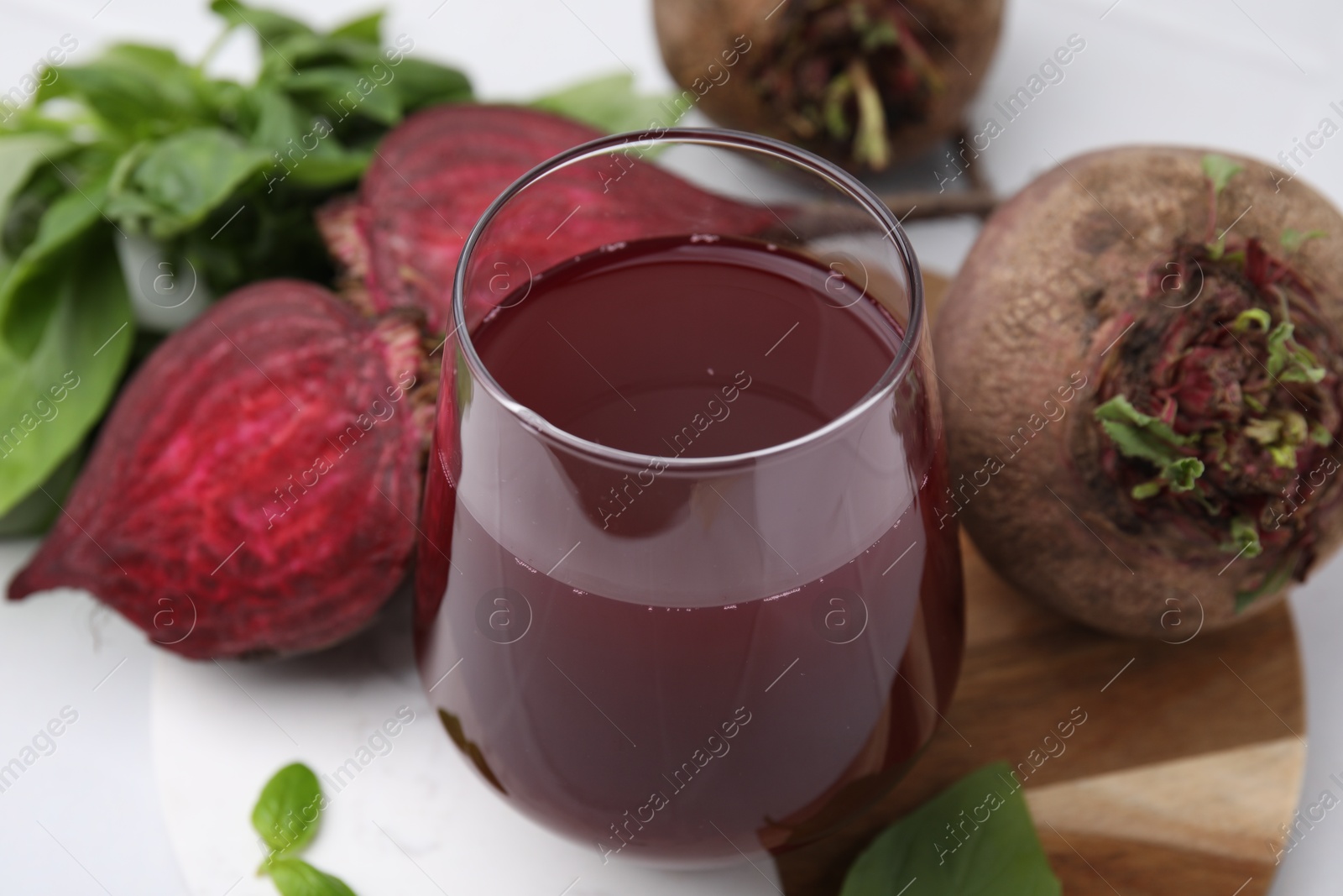 Photo of Fresh beet juice in glass, ripe vegetables and basil on white table, closeup