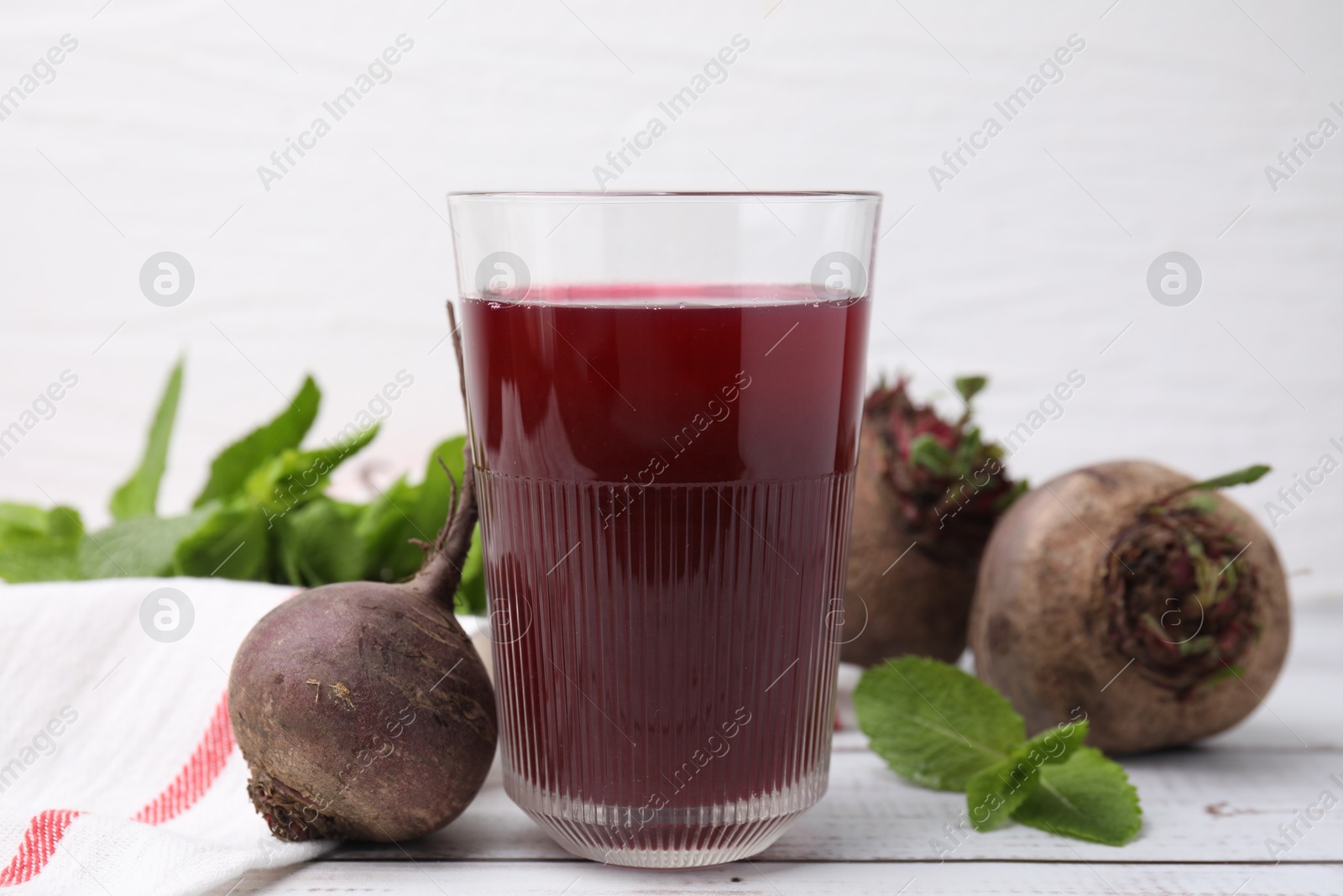 Photo of Fresh beet juice in glass, ripe vegetables and mint on white wooden table, closeup