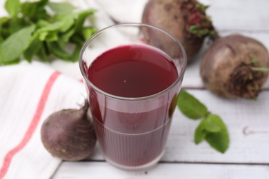 Photo of Fresh beet juice in glass, ripe vegetables and mint on white wooden table, closeup