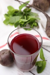 Photo of Fresh beet juice in glass, ripe vegetables and mint on white wooden table, closeup