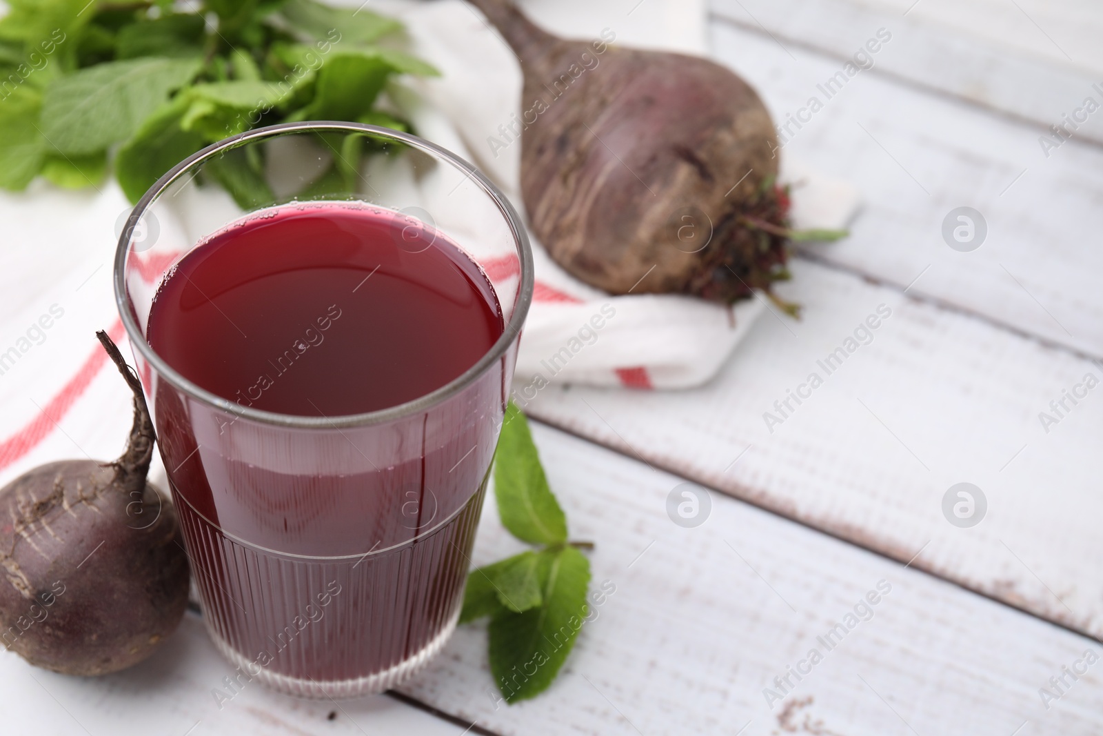 Photo of Fresh beet juice in glass, ripe vegetables and mint on white wooden table, closeup. Space for text