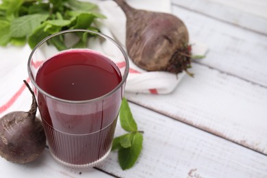 Fresh beet juice in glass, ripe vegetables and mint on white wooden table, closeup. Space for text