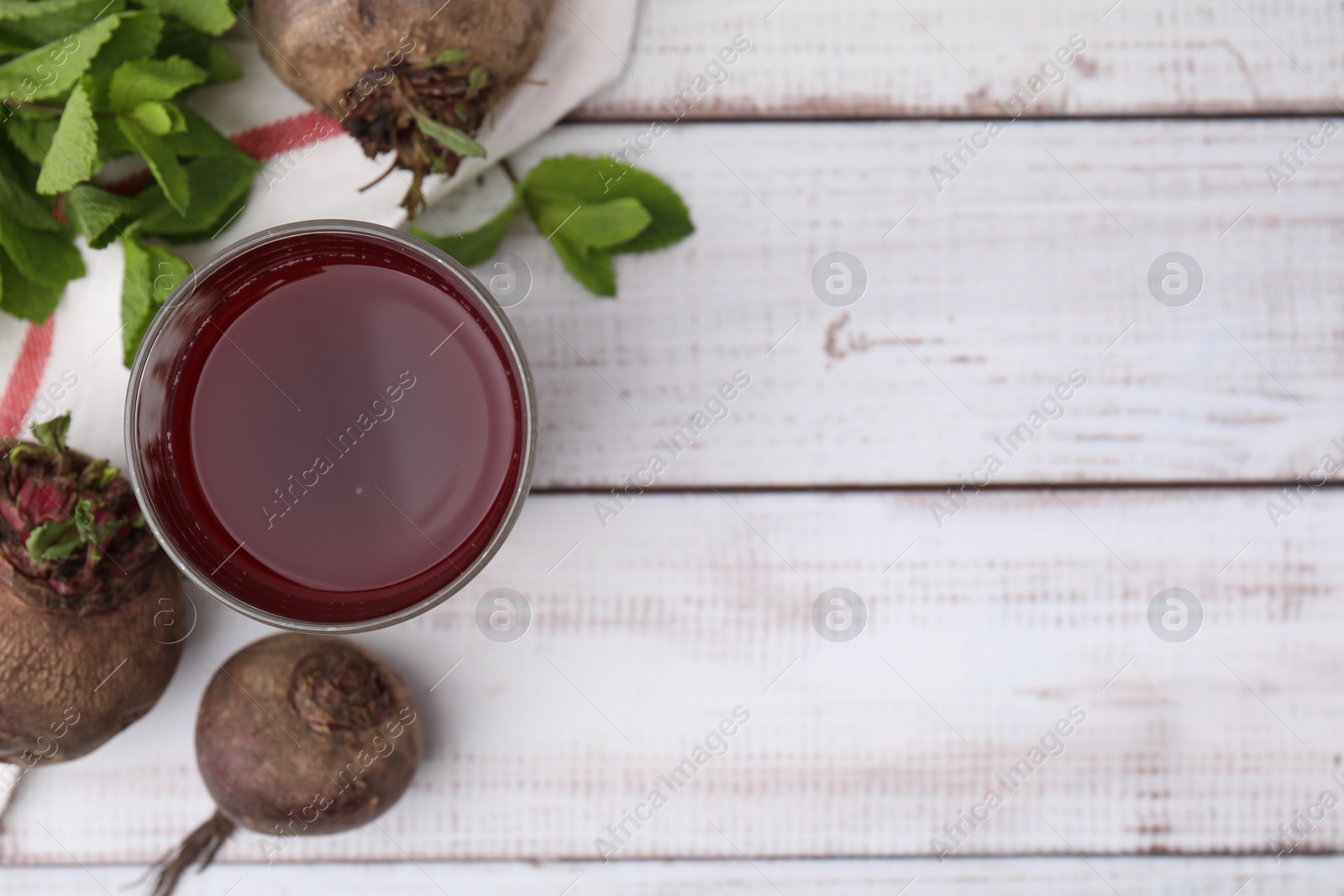 Photo of Fresh beet juice in glass, ripe vegetables and mint on white wooden table, flat lay. Space for text