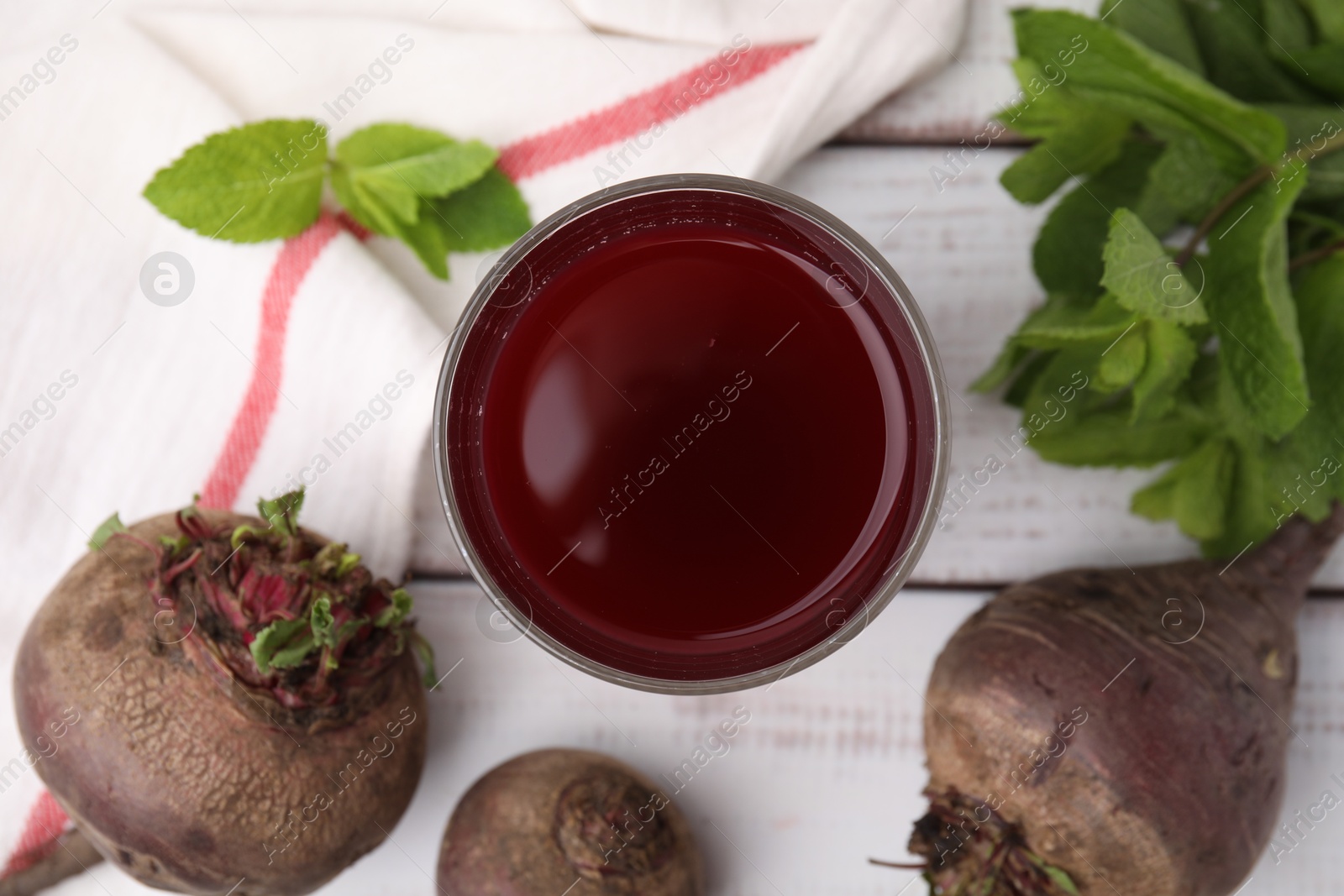 Photo of Fresh beet juice in glass, ripe vegetables and mint on white wooden table, flat lay