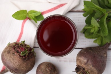 Fresh beet juice in glass, ripe vegetables and mint on white wooden table, flat lay