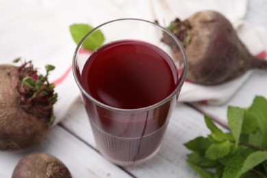 Photo of Fresh beet juice in glass, ripe vegetables and mint on white wooden table, closeup