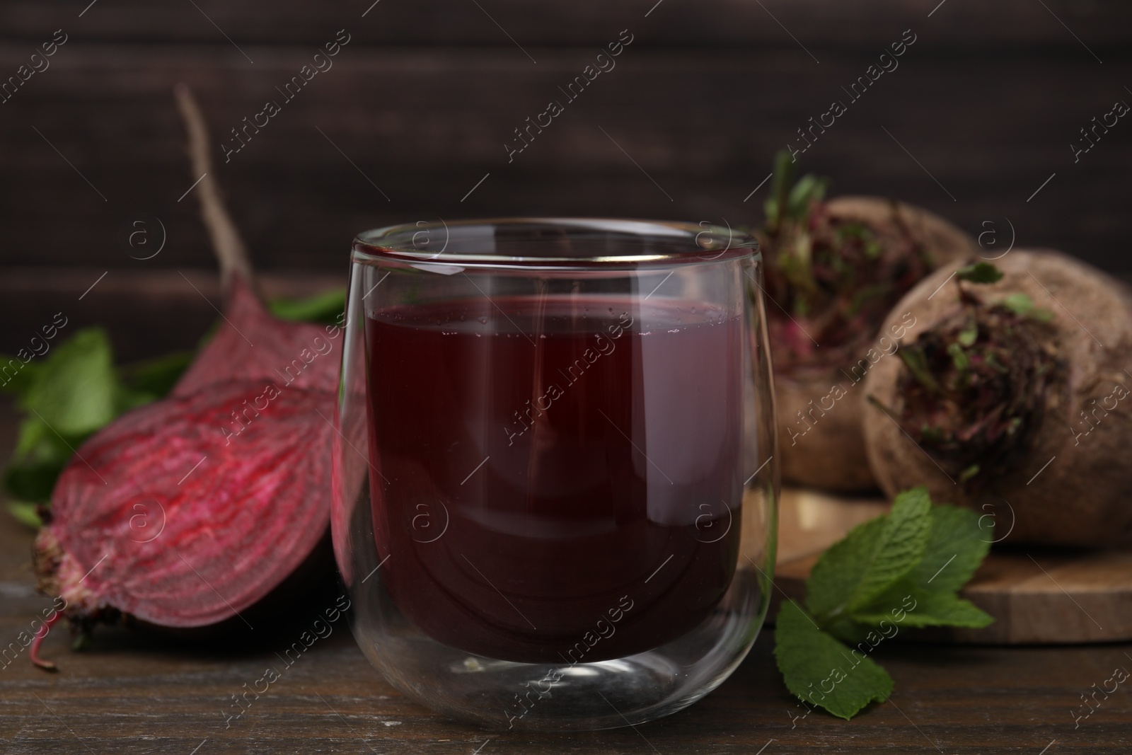 Photo of Fresh beet juice in glass, ripe vegetables and mint on wooden table, closeup