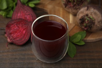 Photo of Fresh beet juice in glass, ripe vegetables and mint on wooden table, closeup