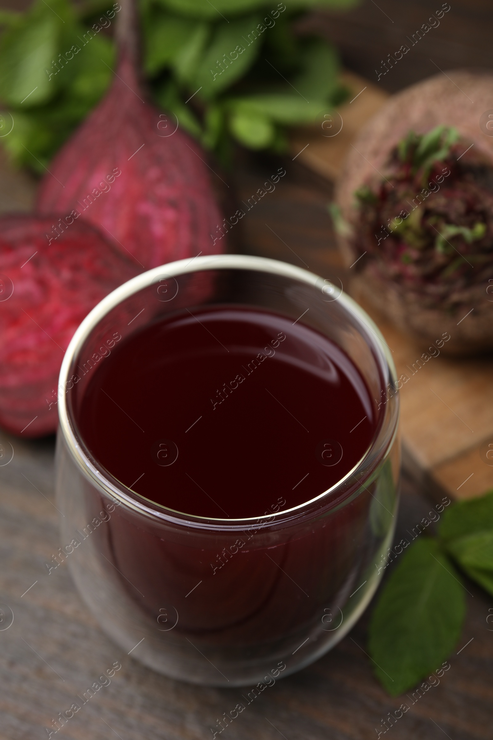 Photo of Fresh beet juice in glass, ripe vegetables and mint on wooden table, closeup