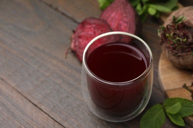 Photo of Fresh beet juice in glass, ripe vegetables and mint on wooden table, closeup. Space for text