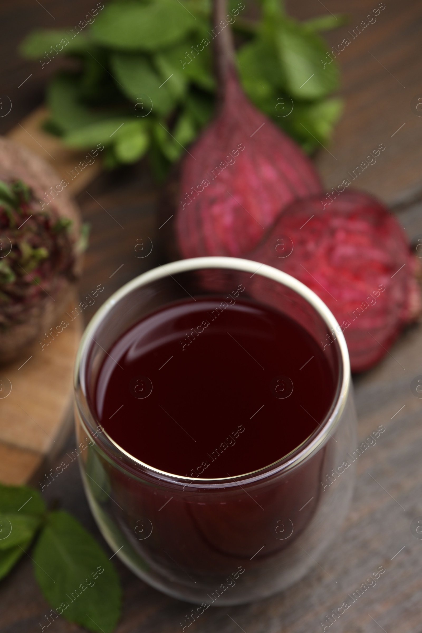 Photo of Fresh beet juice in glass, ripe vegetables and mint on wooden table, closeup