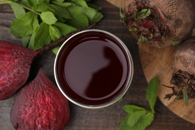 Photo of Fresh beet juice in glass, ripe vegetables and mint on wooden table, flat lay