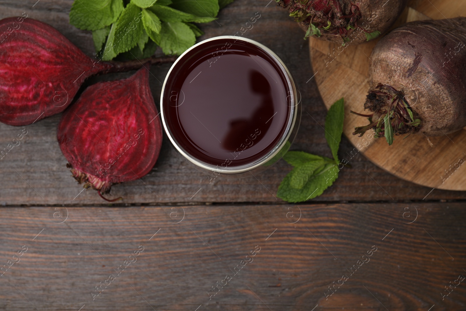 Photo of Fresh beet juice in glass, ripe vegetables and mint on wooden table, flat lay. Space for text