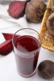 Photo of Fresh beet juice in glass and ripe vegetables on white table, closeup