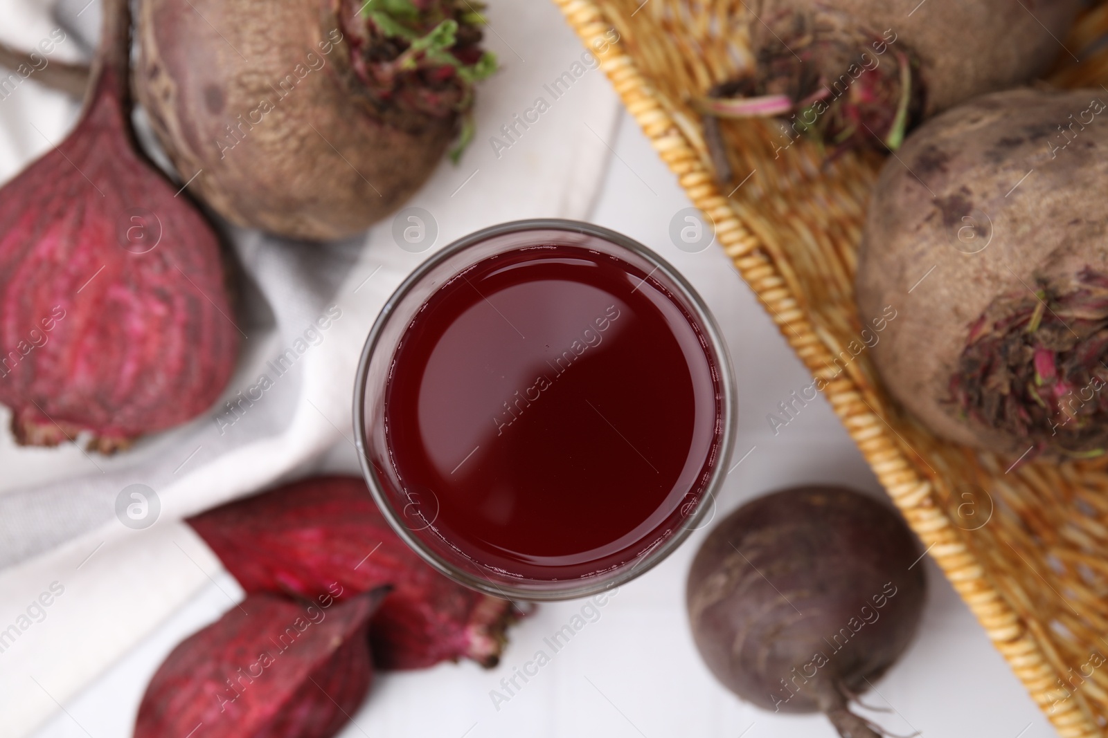 Photo of Fresh beet juice in glass and ripe vegetables on white table, flat lay