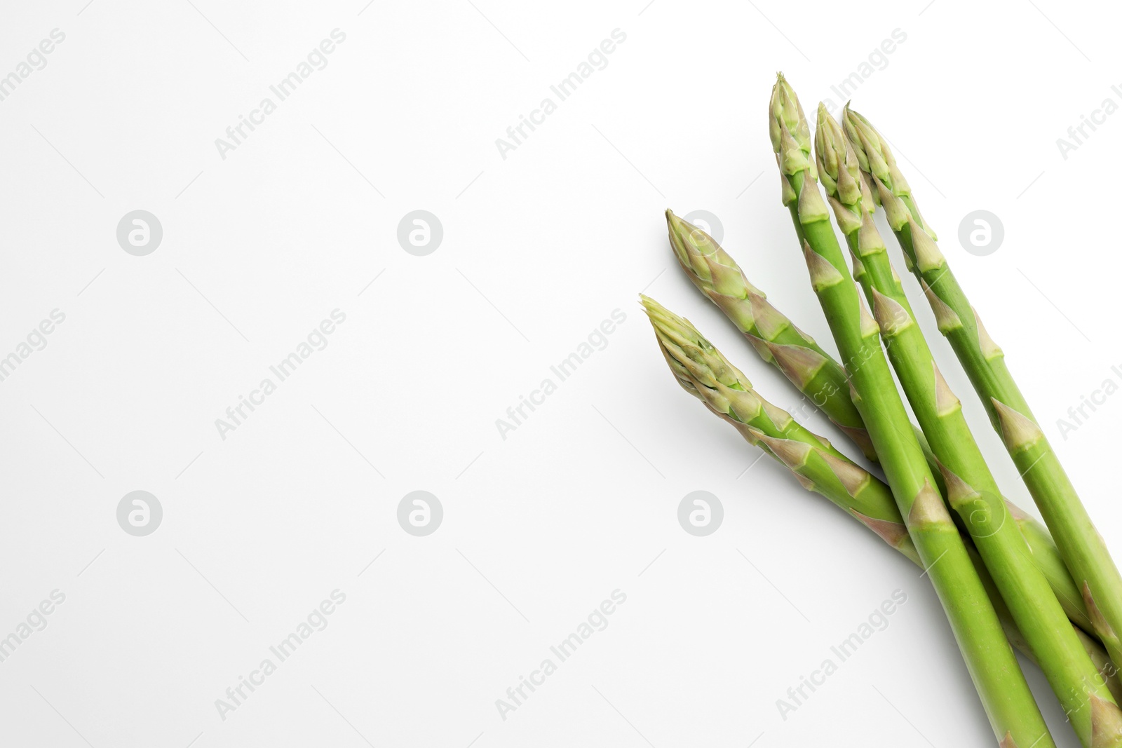 Photo of Fresh green asparagus stems on white background, top view. Space for text