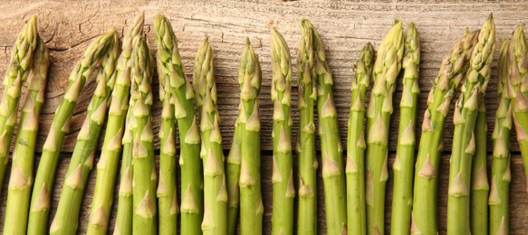 Photo of Fresh green asparagus stems on wooden table, flat lay