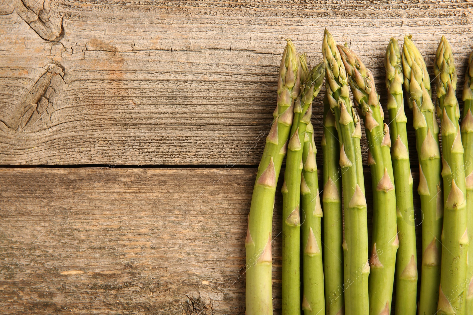 Photo of Fresh green asparagus stems on wooden table, flat lay. Space for text