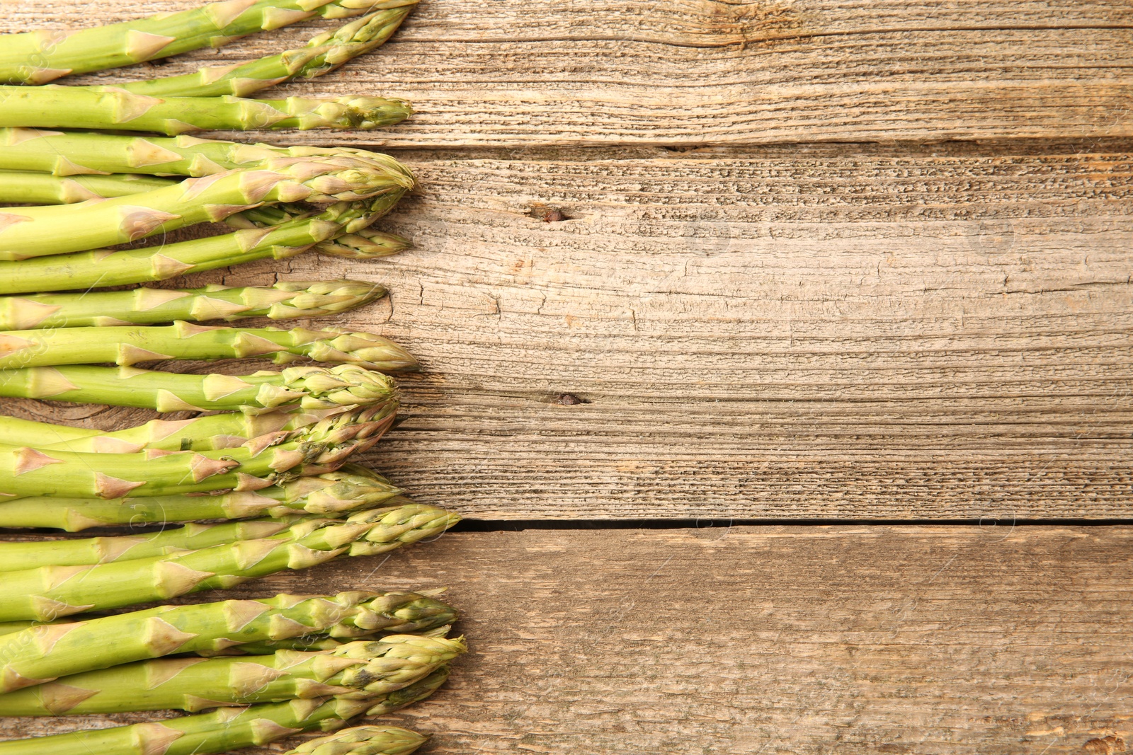 Photo of Fresh green asparagus stems on wooden table, flat lay. Space for text