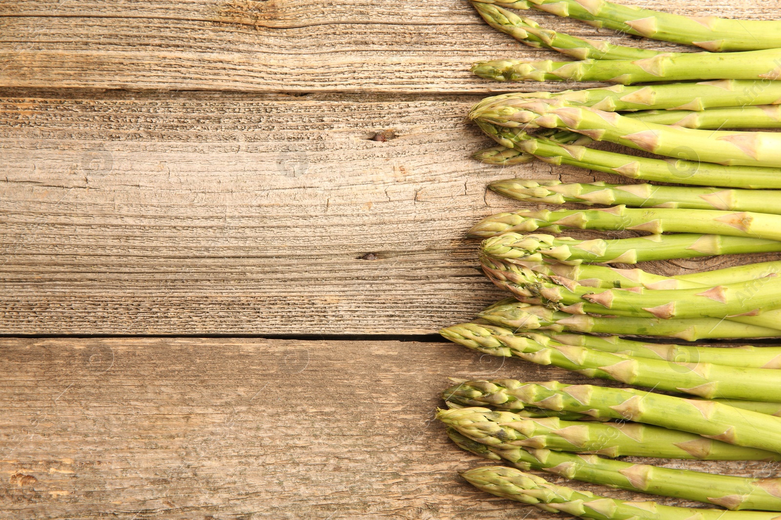 Photo of Fresh green asparagus stems on wooden table, flat lay. Space for text