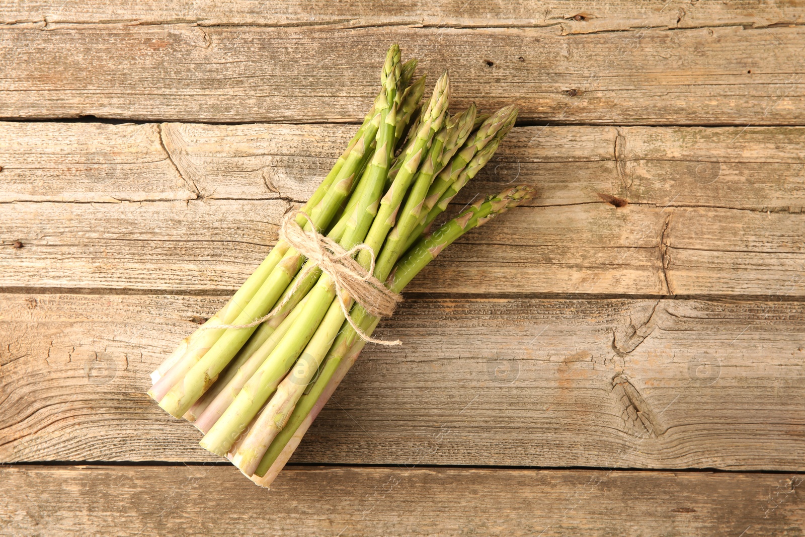 Photo of Bunch of fresh green asparagus stems on wooden table, top view