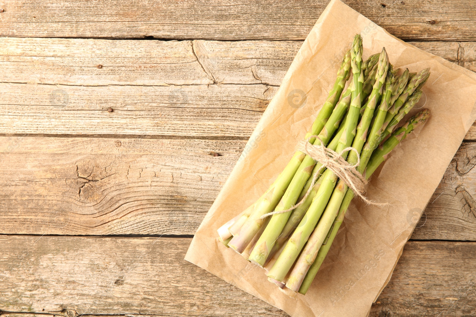 Photo of Bunch of fresh green asparagus stems on wooden table, top view. Space for text