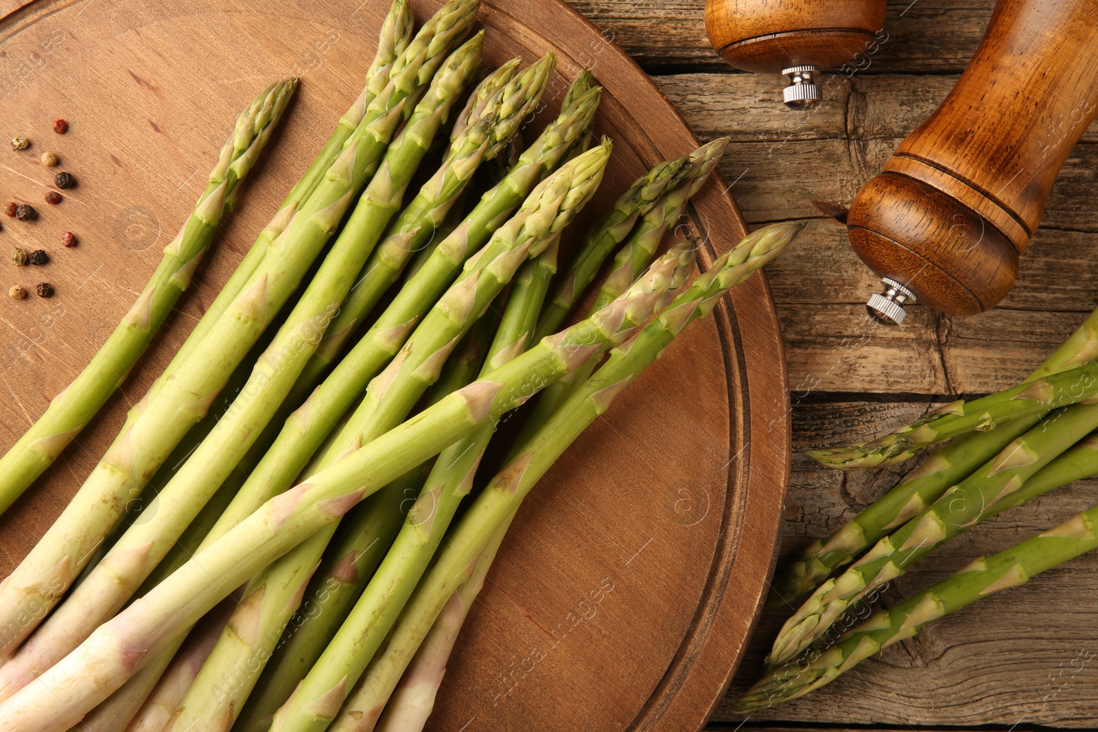 Photo of Board with fresh green asparagus stems and shakers on wooden table, flat lay