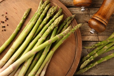 Photo of Board with fresh green asparagus stems and shakers on wooden table, flat lay