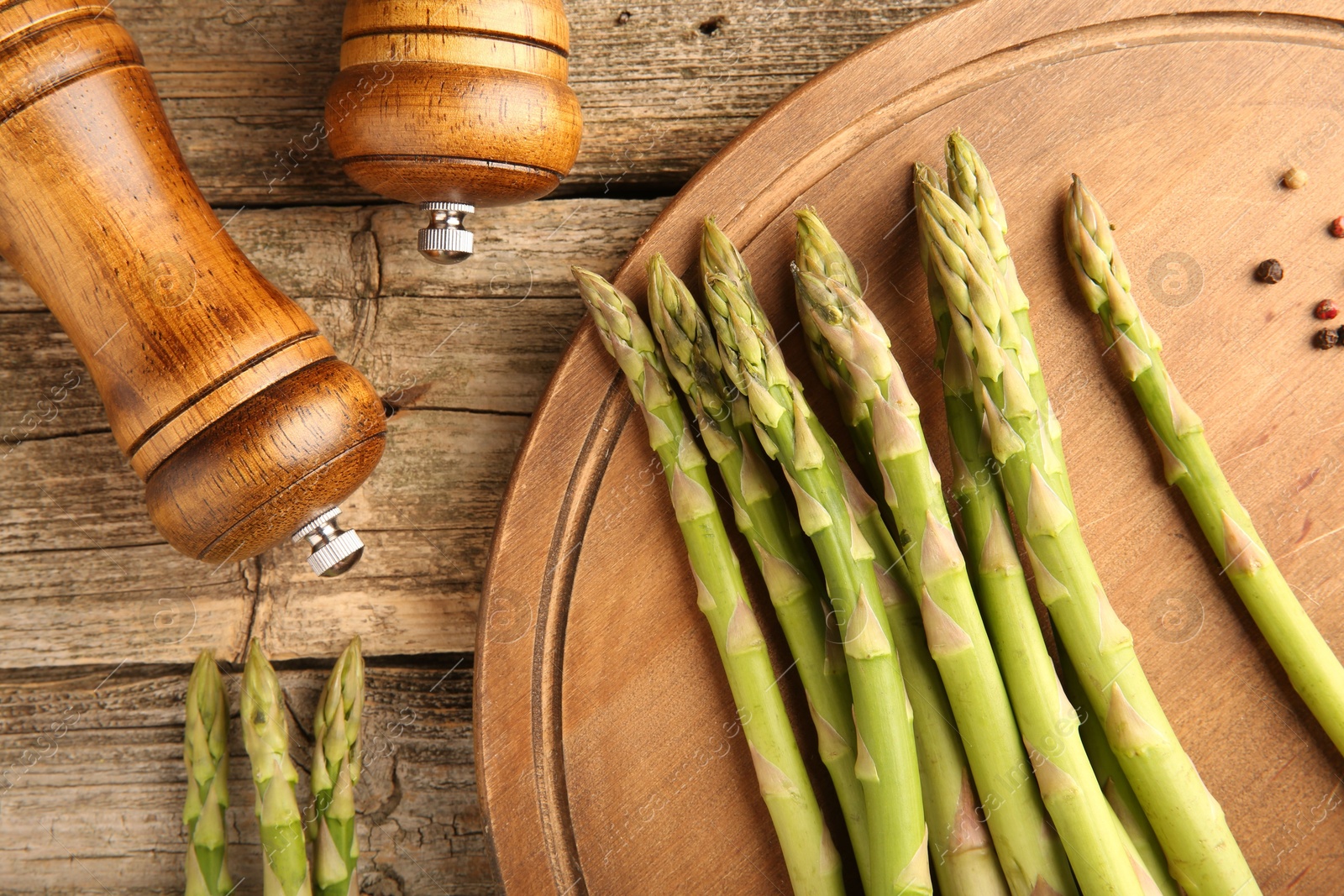 Photo of Board with fresh green asparagus stems and shakers on wooden table, flat lay