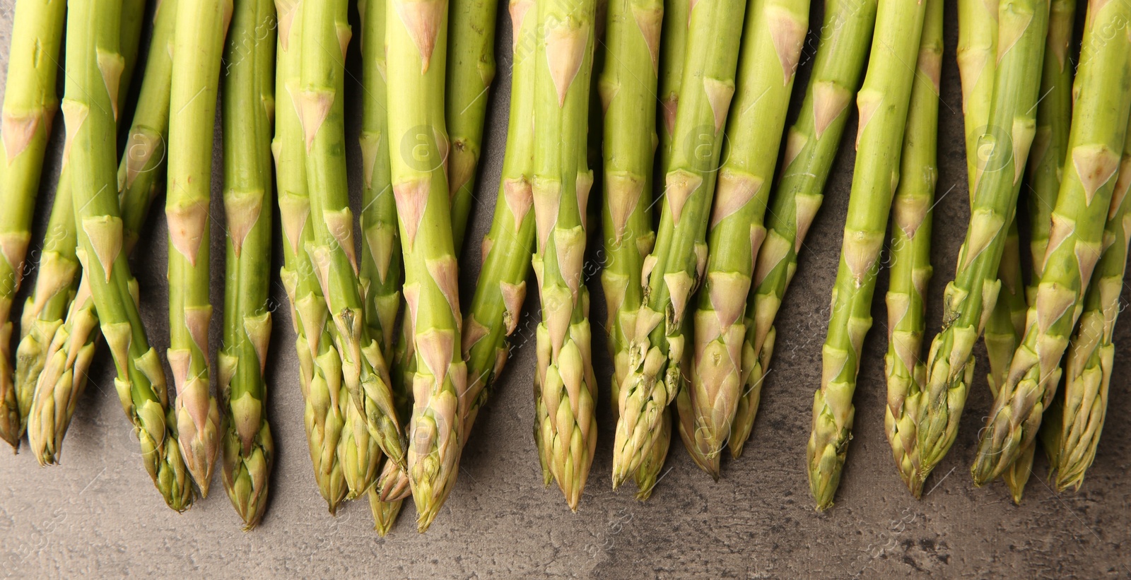 Photo of Fresh green asparagus stems on grey textured table, flat lay