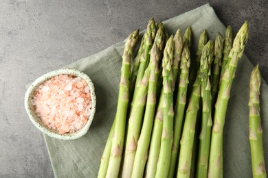 Photo of Fresh green asparagus stems and sea salt on grey textured table, top view